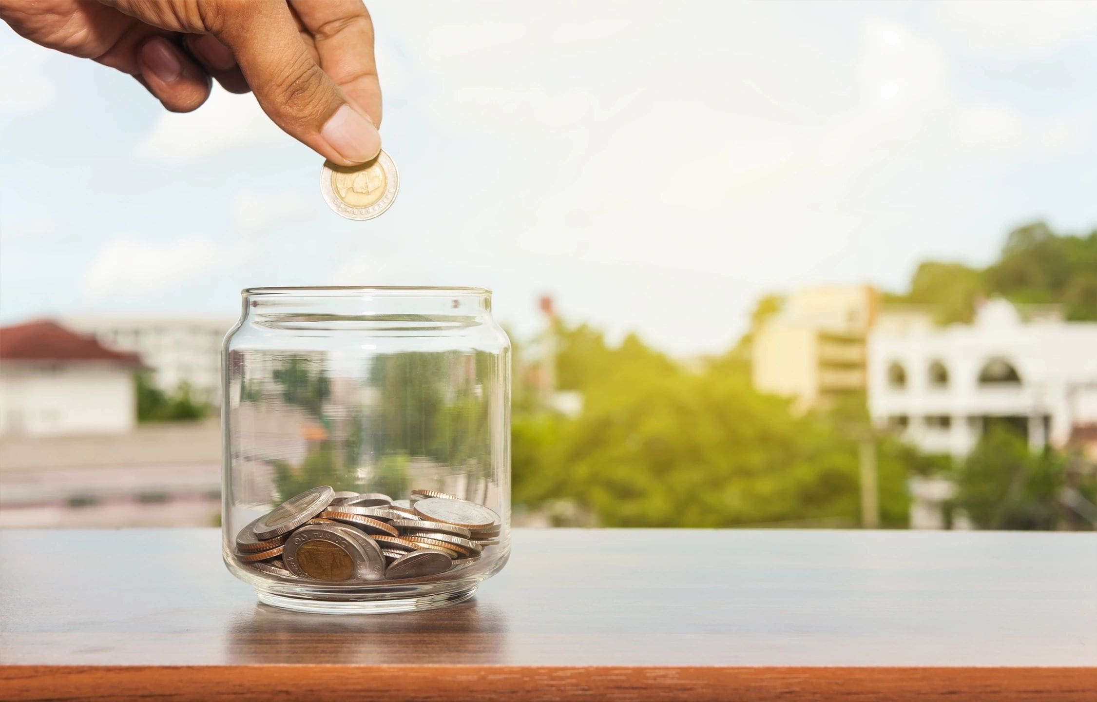 A person is putting money in a glass jar.